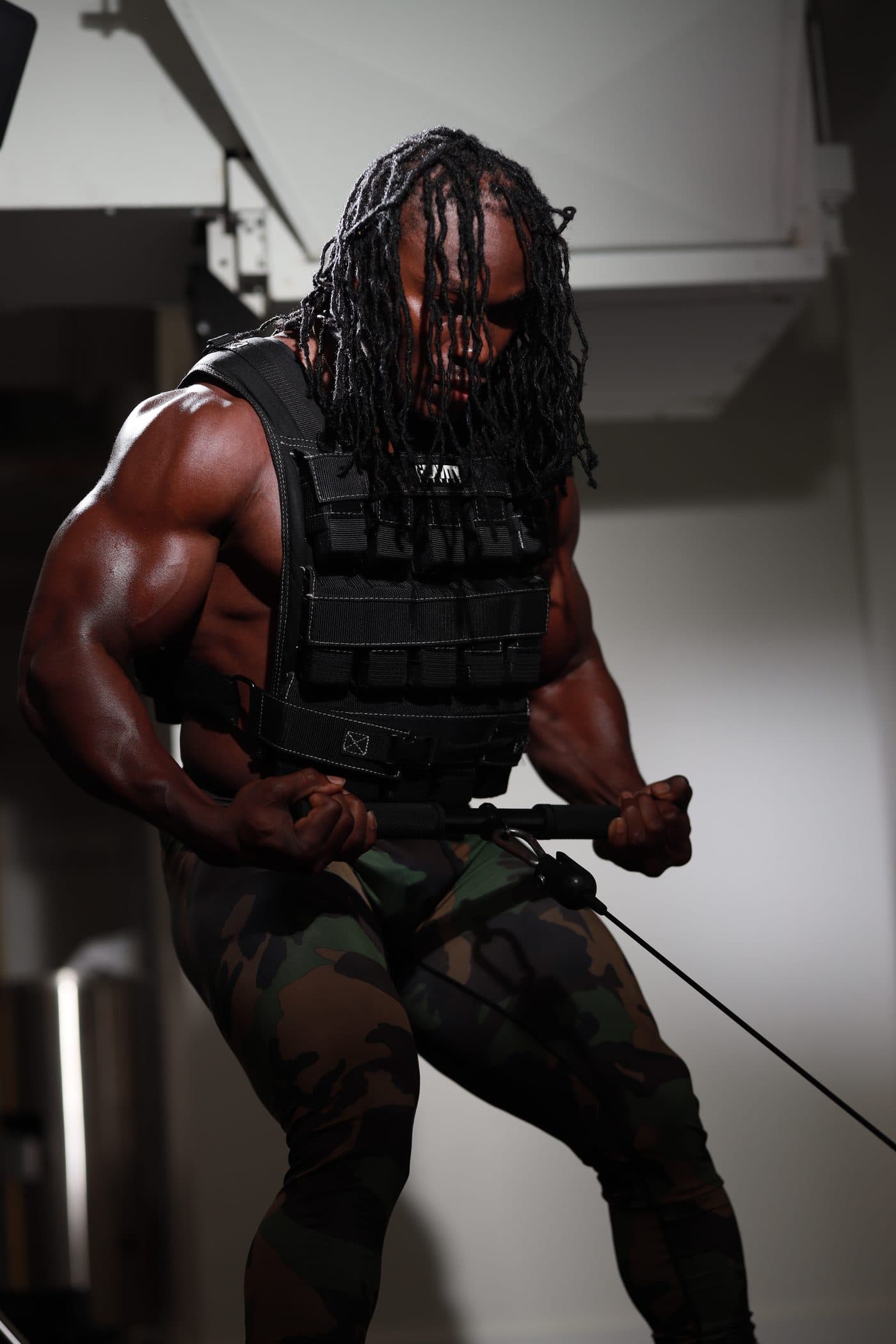 Alseny Sylla in a weighted training vest pulling a cable resistance handle during a strength session
